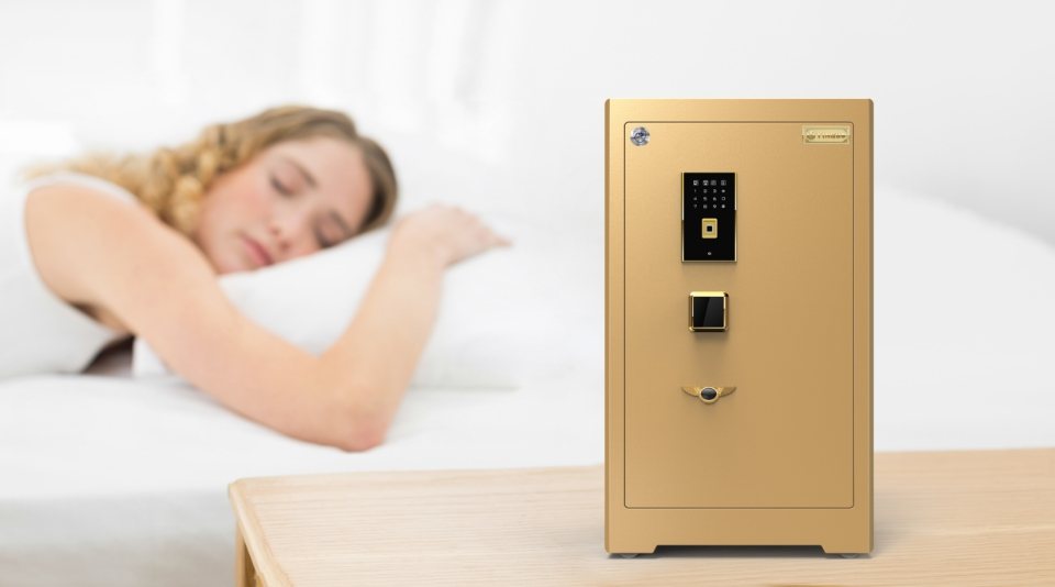 A gold home safe is placed on the desk with a girl sleeping aside.