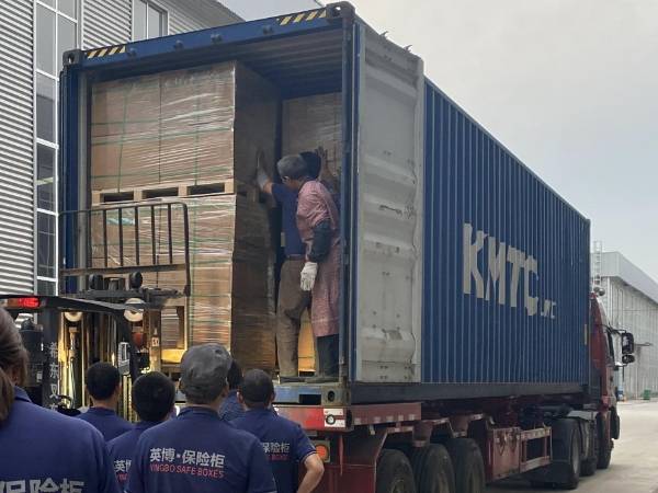 Varios trabajadores están cargando cajas fuertes en contenedores.